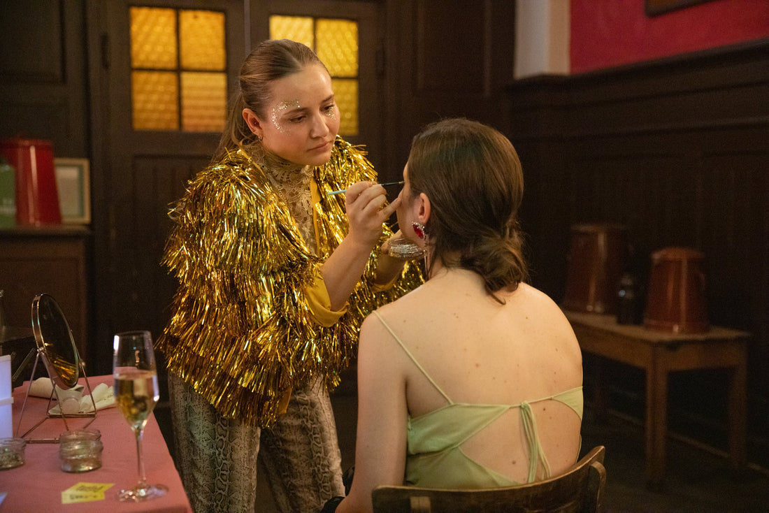 makeup artist wearing sequin cape applying glitter to a guest