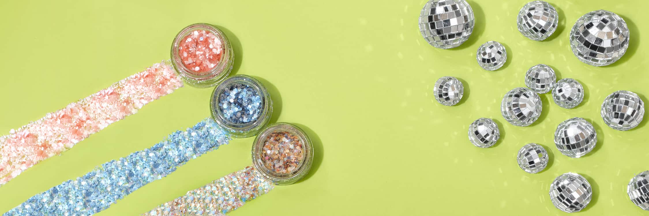 Three pots of glitter and decorative disco balls on a green background