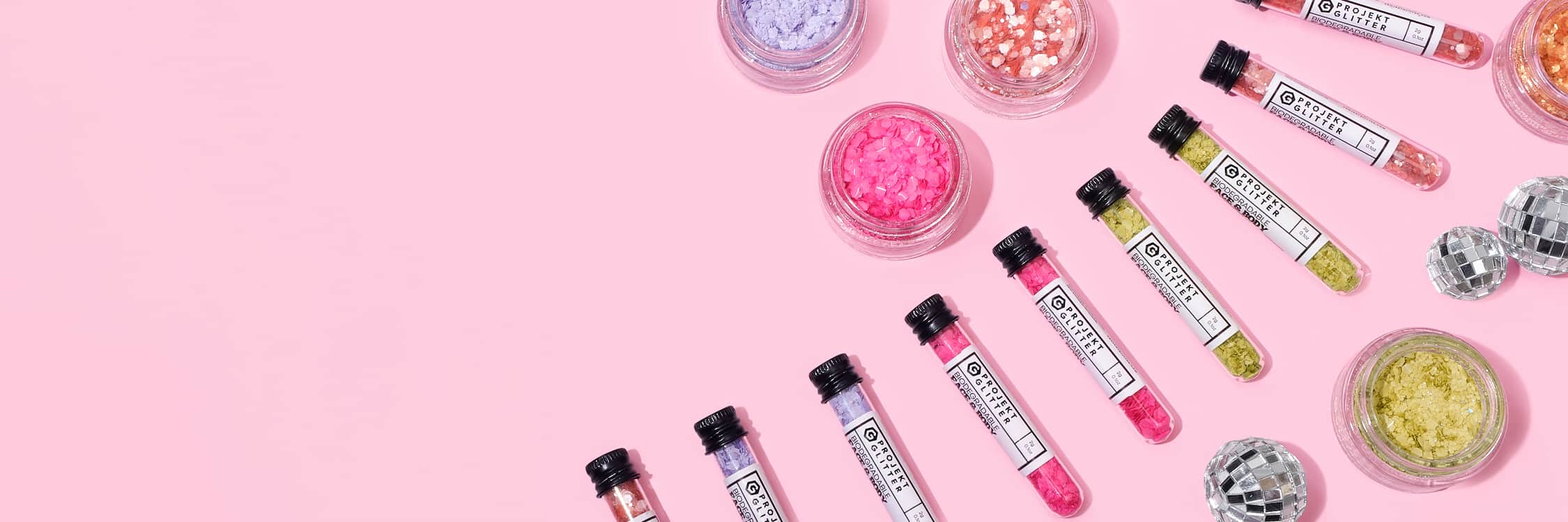 Collection of small glitter tubes with colorful contents on a pink background