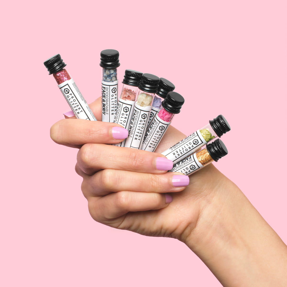 Hand holding multiple small tubes against a pink background