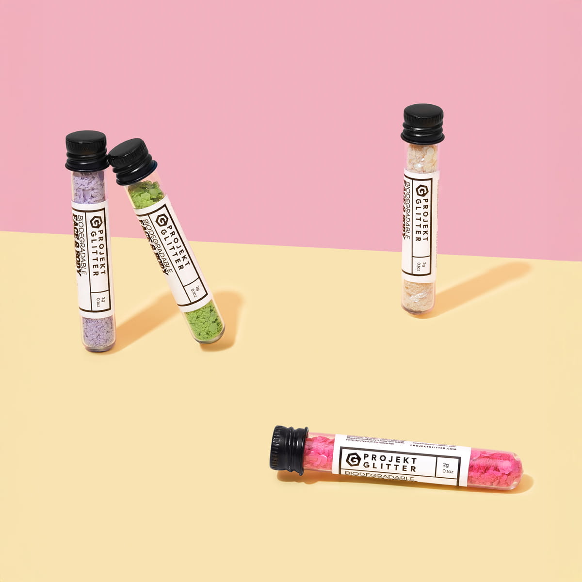 Four small cylindrical containers of glitter with labels on a pink and beige background
