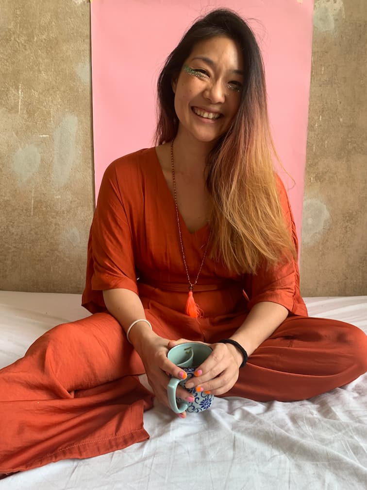 Woman in orange outfit holding a mug against a pink and gold background